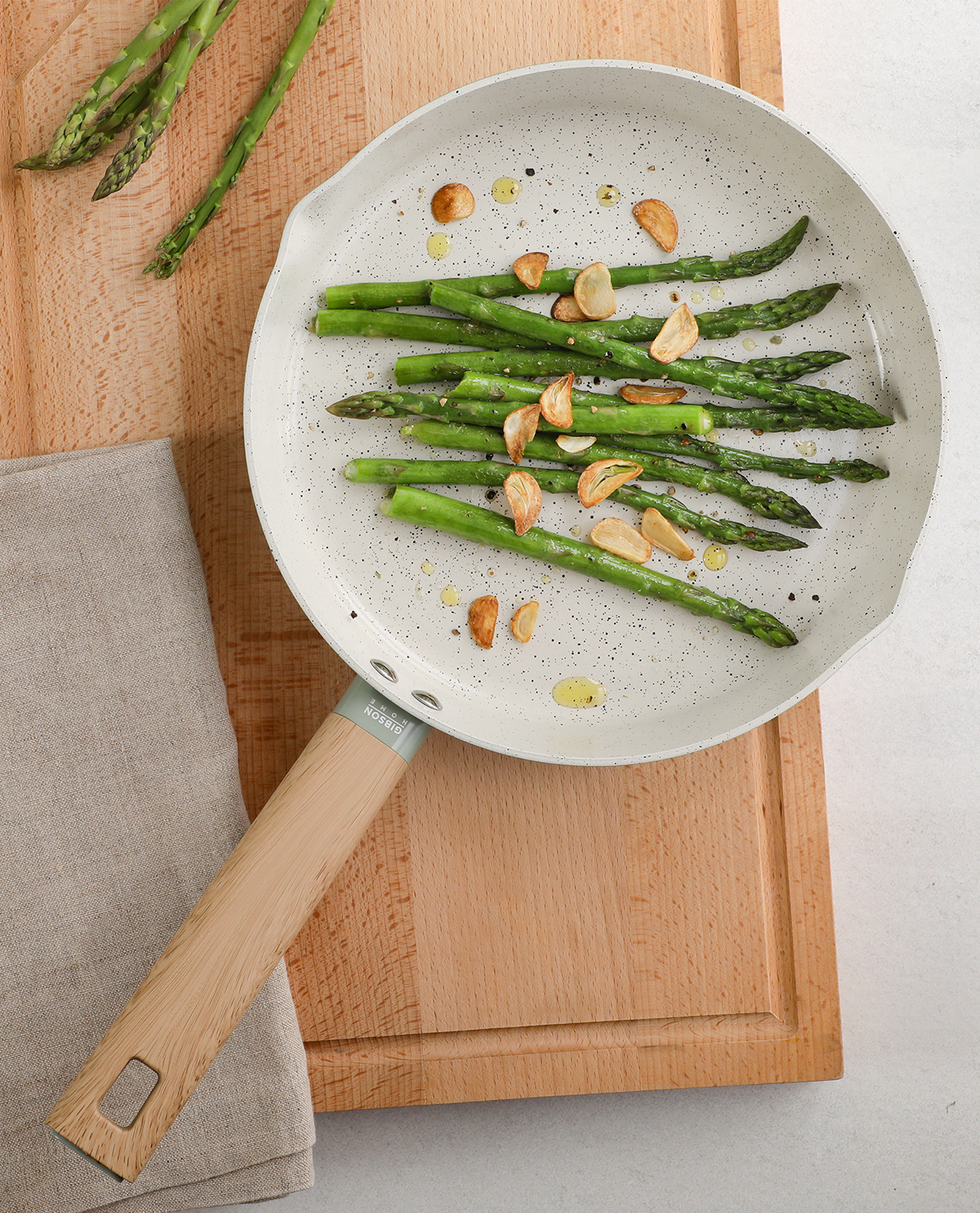 Frying pan with asparagus and garlic on a wooden cutting board