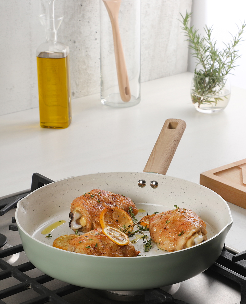 Cooked chicken in a pan on a stove with ingredients in the background