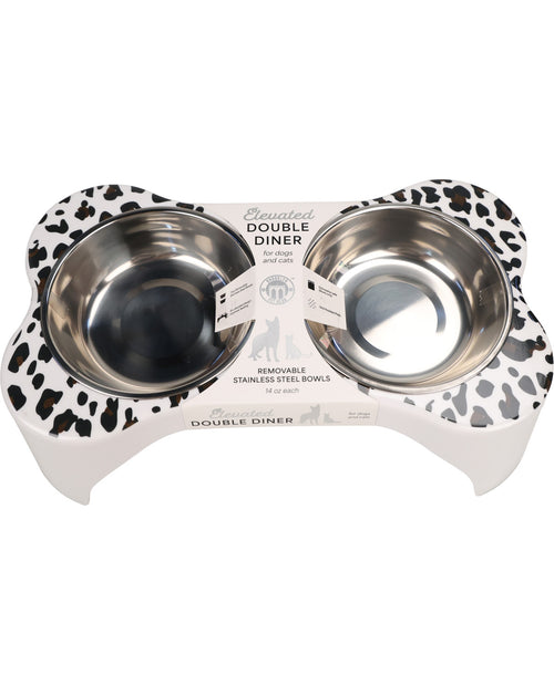 A pet double-diner bowl set featuring two stainless steel bowls set into a white elevated base with a black and white cow-print pattern, shown on a white background.