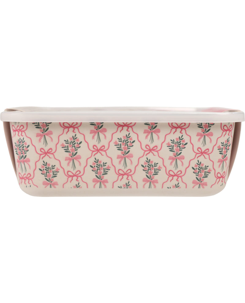 A rectangular ceramic baking pan with a white lid, featuring a pink and green floral pattern with bows on a cream-colored exterior.