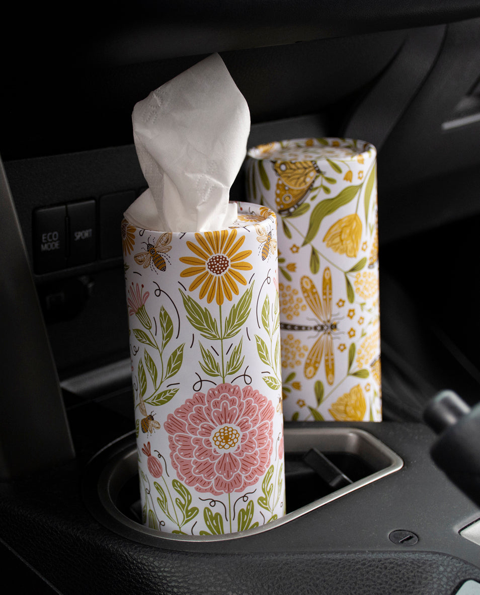 Floral-patterned tissue box and roll in a car's cup holder.