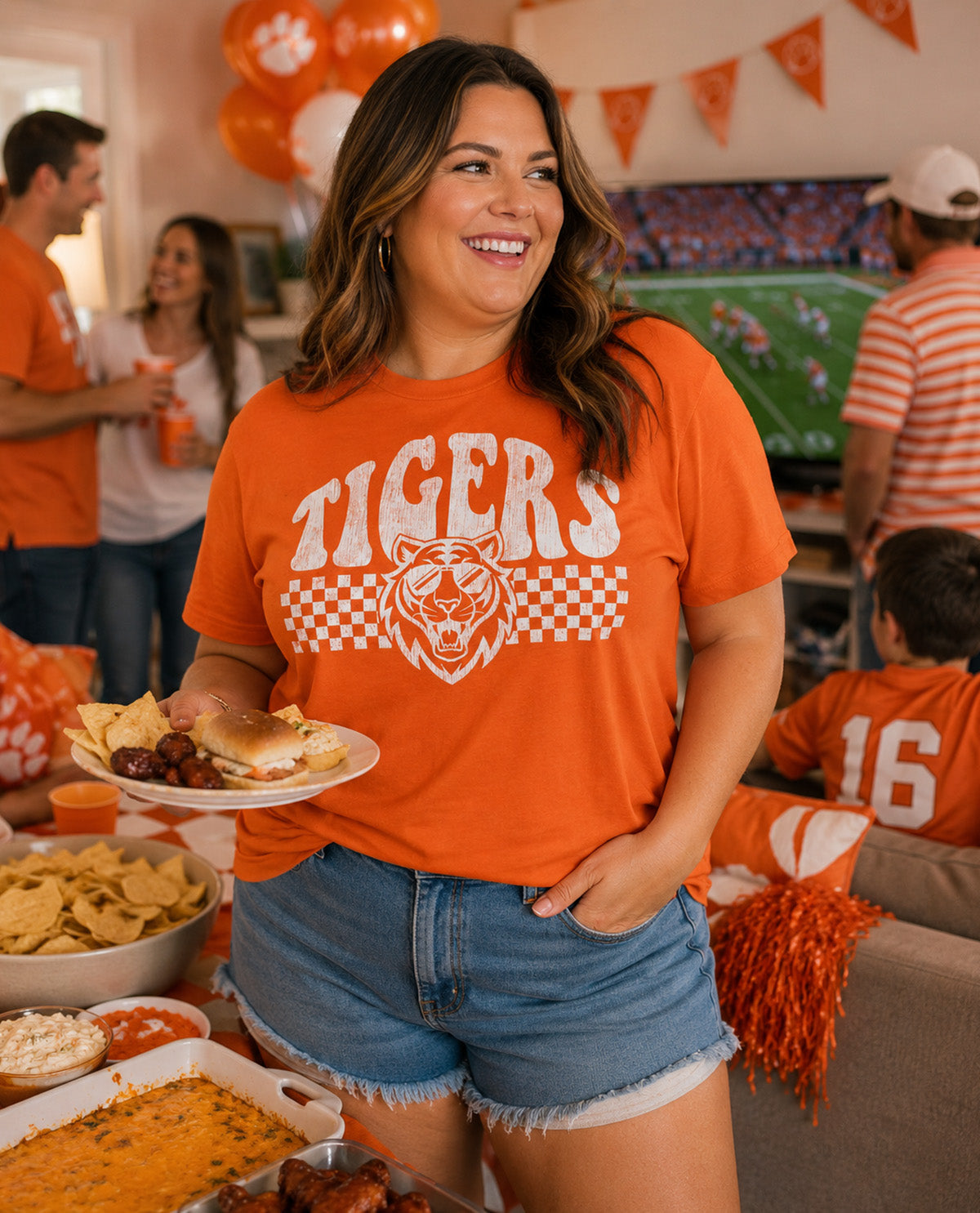 Woman in orange 'Tigers' shirt holding a plate of food at a sports event gathering.