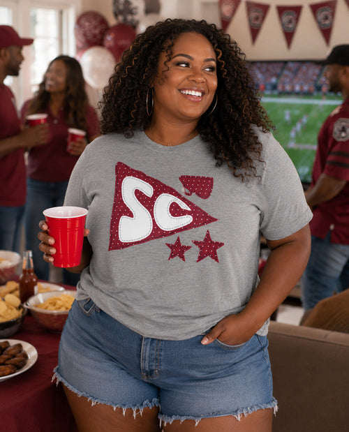 Woman wearing a gray t-shirt with a logo, holding a red cup in a casual setting.