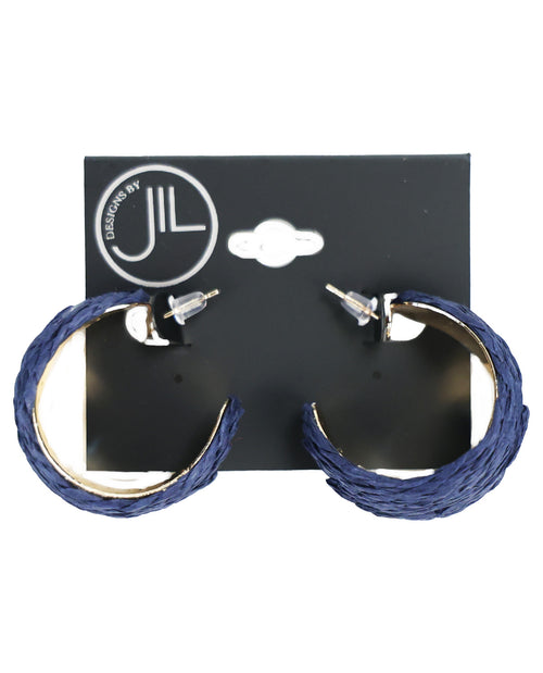 A pair of thick, textured blue hoop earrings with silver-tone posts, displayed on a black hanging card featuring the 'JIL DESIGNS BY' logo, set against a plain white background.