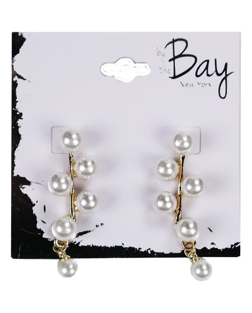 A pair of gold-tone dangle earrings with white faux pearls, displayed on a white and black 'by the Bay New York' retail card.