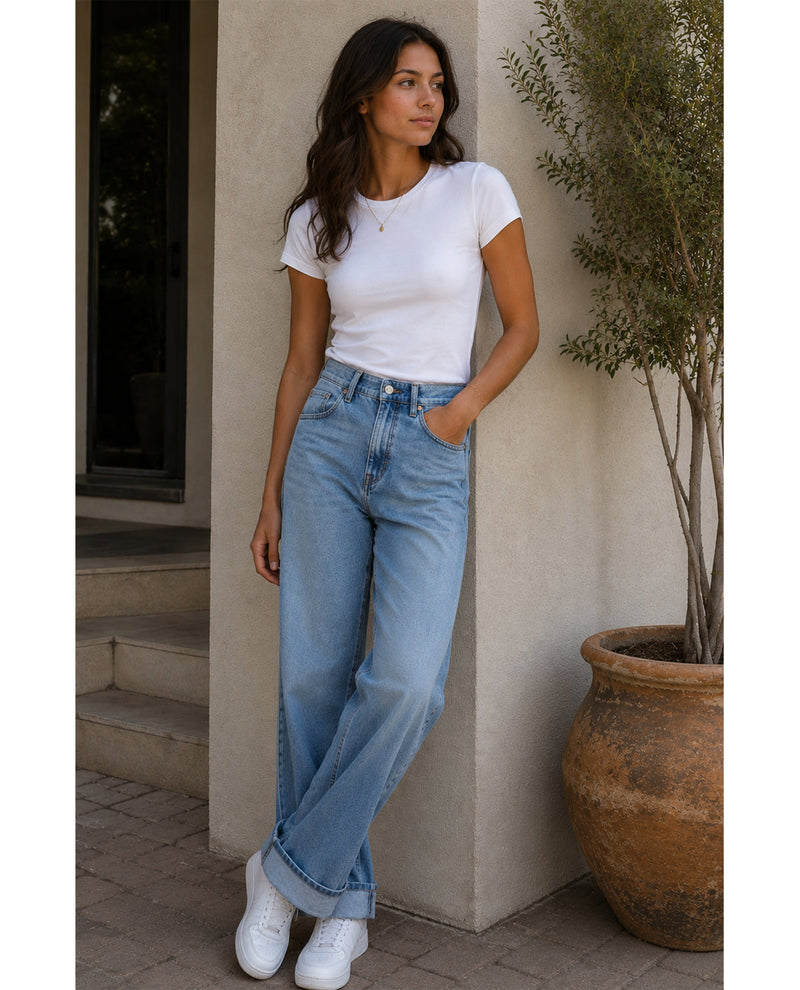 Woman wearing a white t-shirt and blue jeans standing against a beige wall.