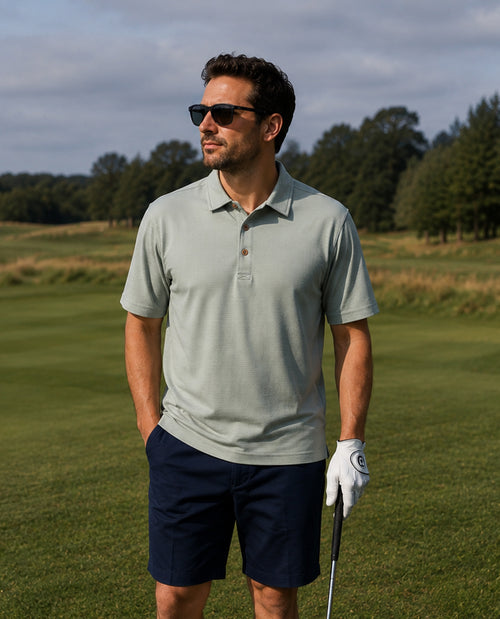 Man on a golf course wearing sunglasses and a light gray polo shirt.
