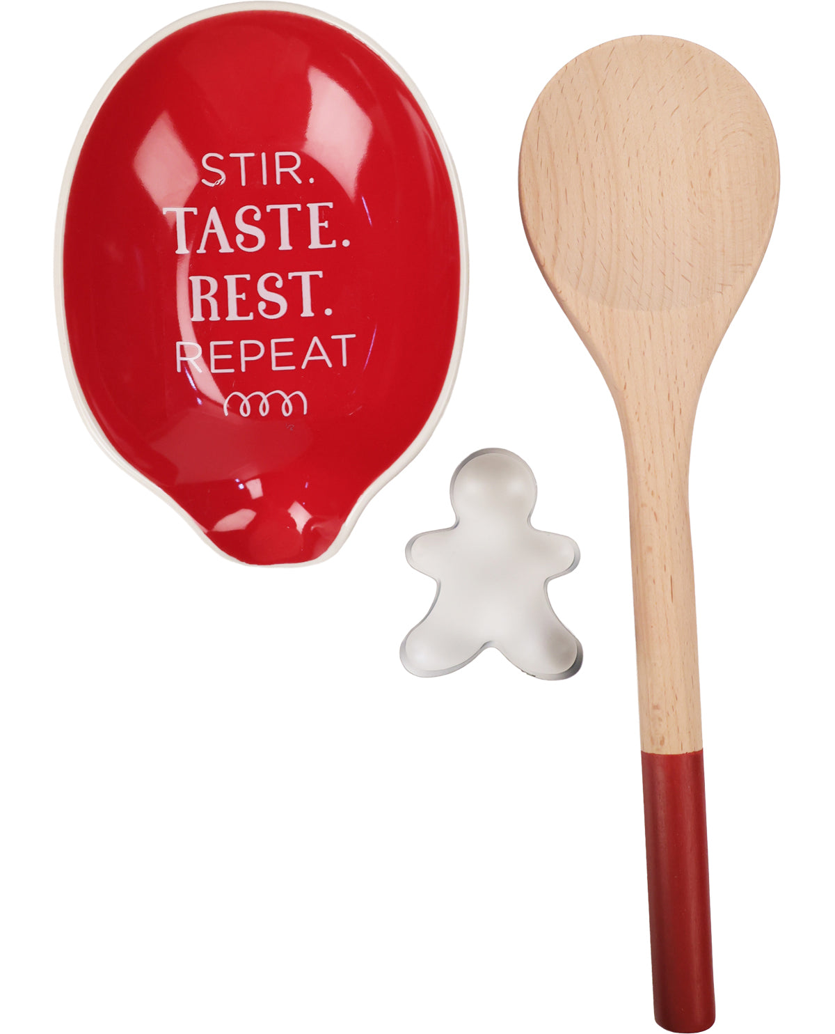 A kitchen utensil set featuring a glossy red ceramic spoon rest with white text, a natural wood spoon with a red-painted handle, and a small gingerbread-shaped metal cookie cutter, all on a white background.