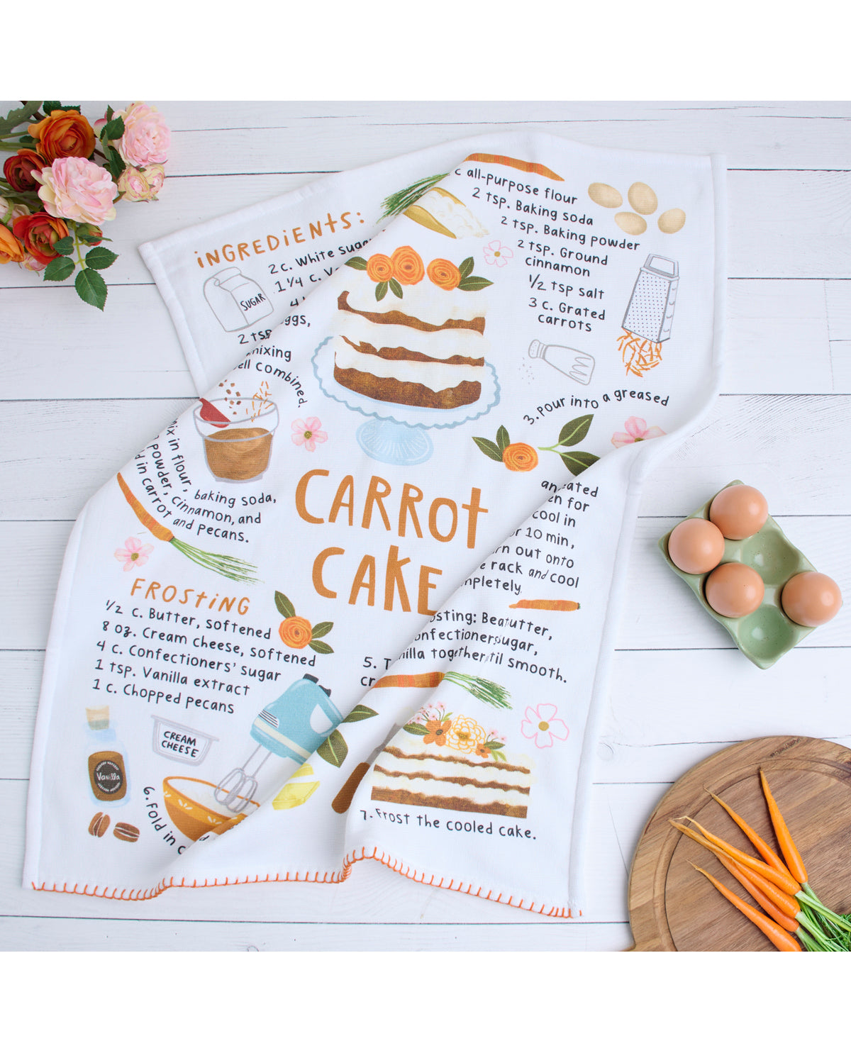 Carrot cake-themed kitchen towel with recipe illustration on a wooden surface.