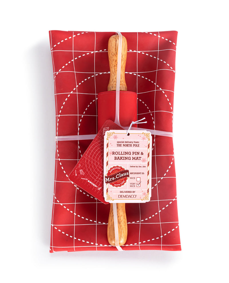 A red rolling pin and matching red baking mat set wrapped in a red grid-patterned gift wrap, tied with a string and featuring a paper tag from Mrs. Claus's.