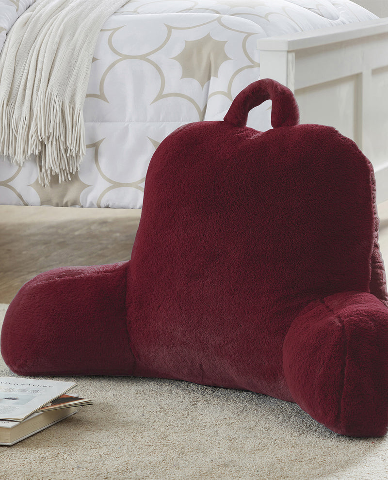 Red backrest pillow on a carpeted floor with a patterned wall in the background