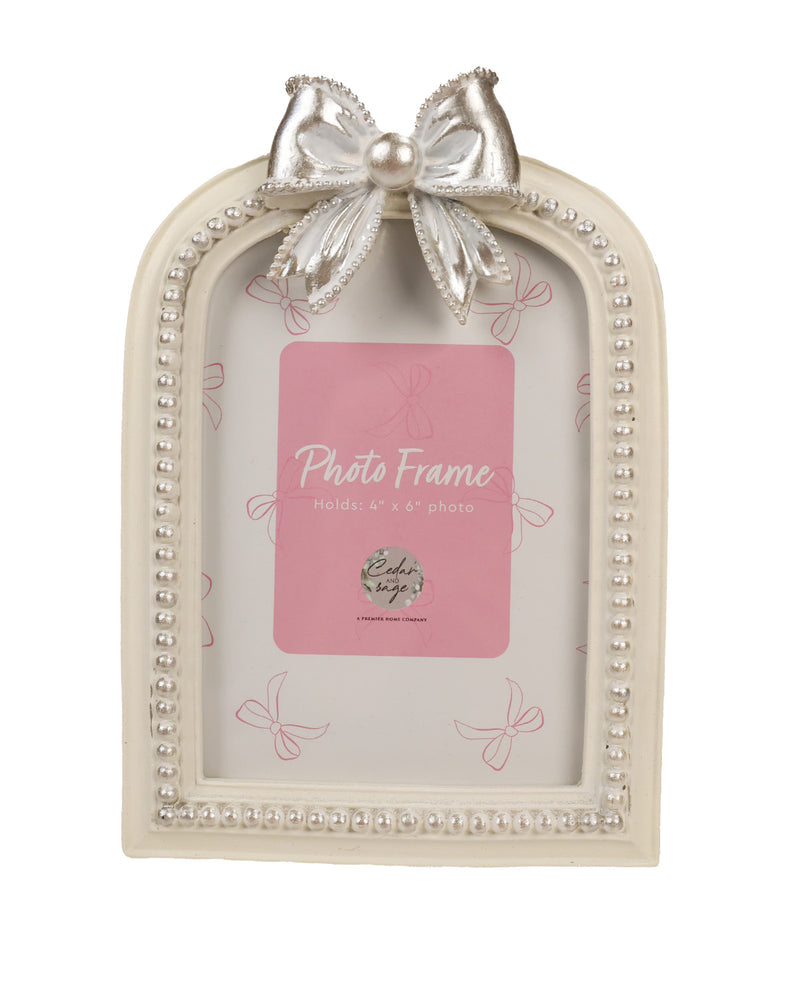An arched cream-colored picture frame with a decorative silver bow and pearl-like beaded border, shown holding a pink placeholder card.