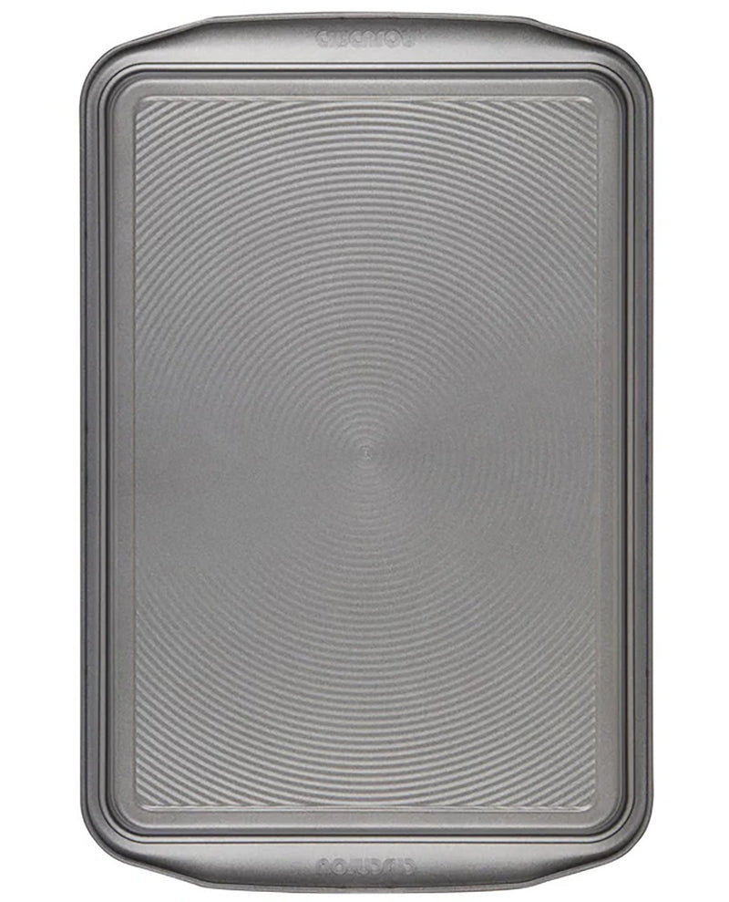 A rectangular metal baking pan with rounded corners and a textured, concentric-circle pattern on the bottom half, shown against a plain white background.
