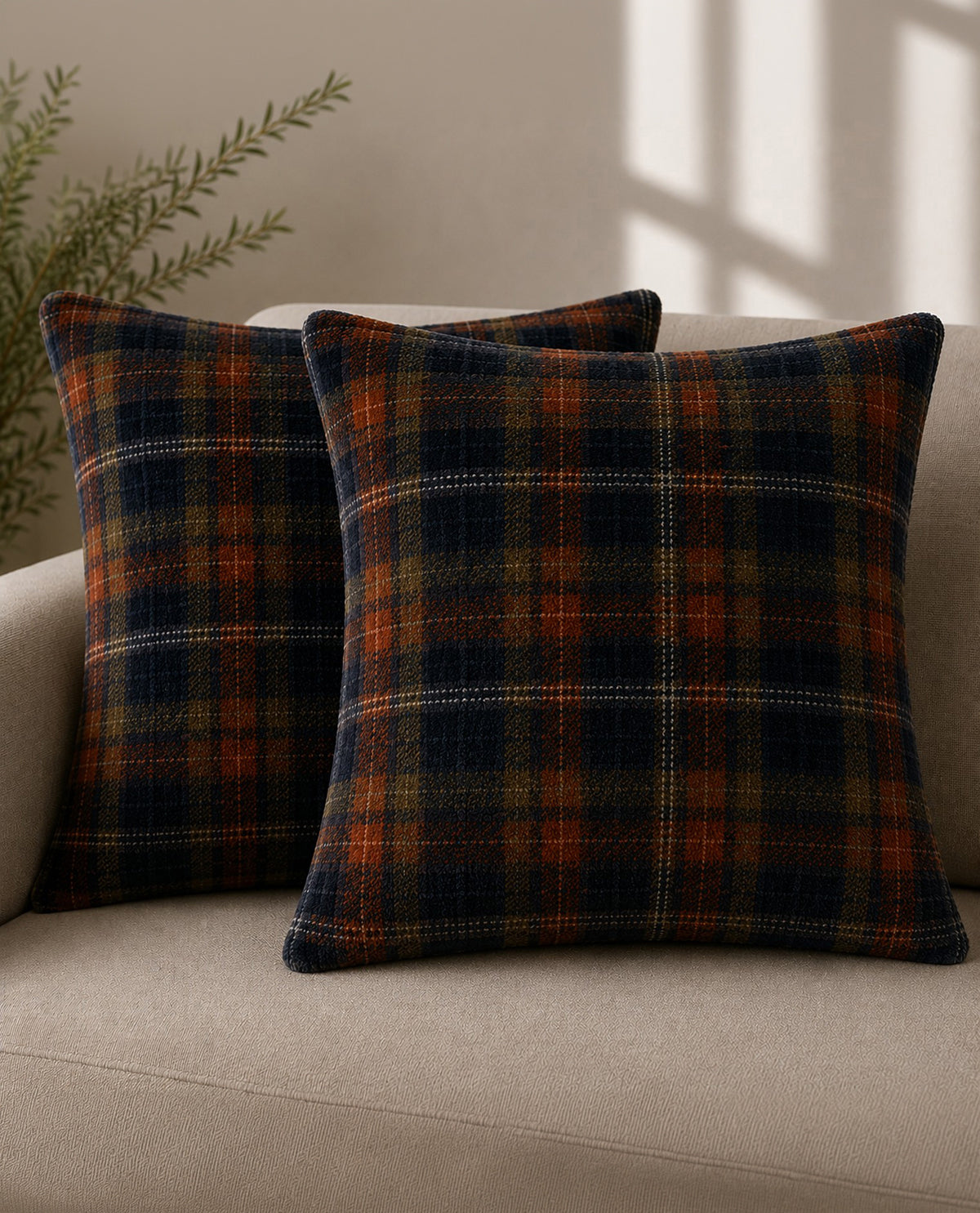 Two plaid pillows on a beige couch with a neutral background