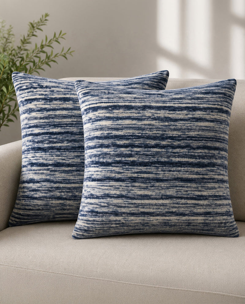 Two blue patterned pillows on a beige sofa with a plant in the background.