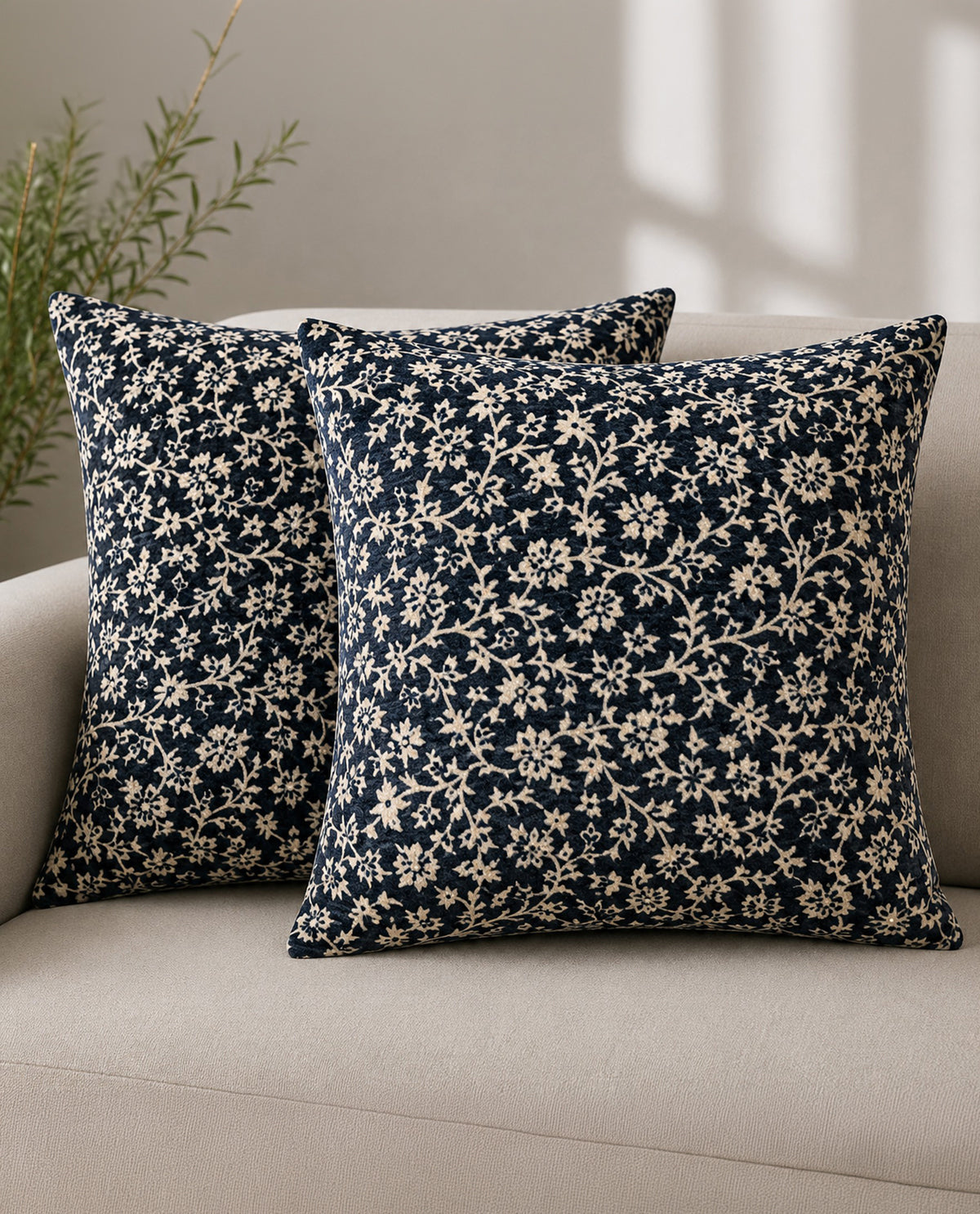 Two navy blue floral patterned pillows on a beige sofa.