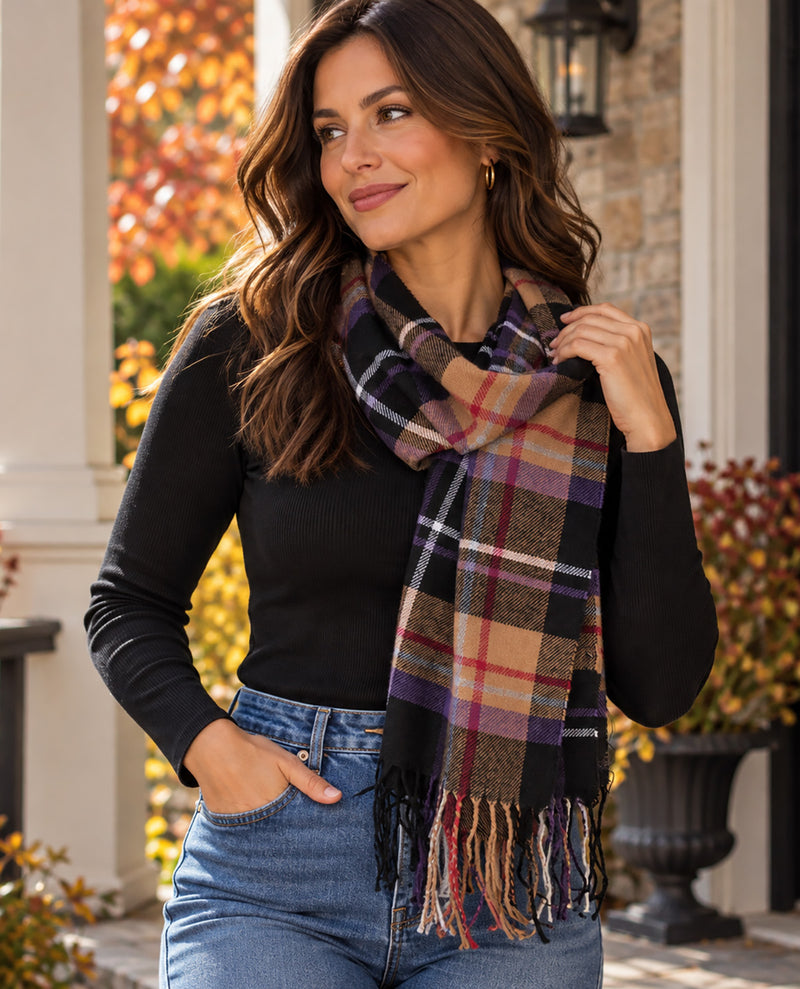 A woman wearing a black long-sleeve top and blue jeans models a large plaid scarf with fringe. The scarf features a multicolor pattern of black, beige, purple, red, and white plaid.