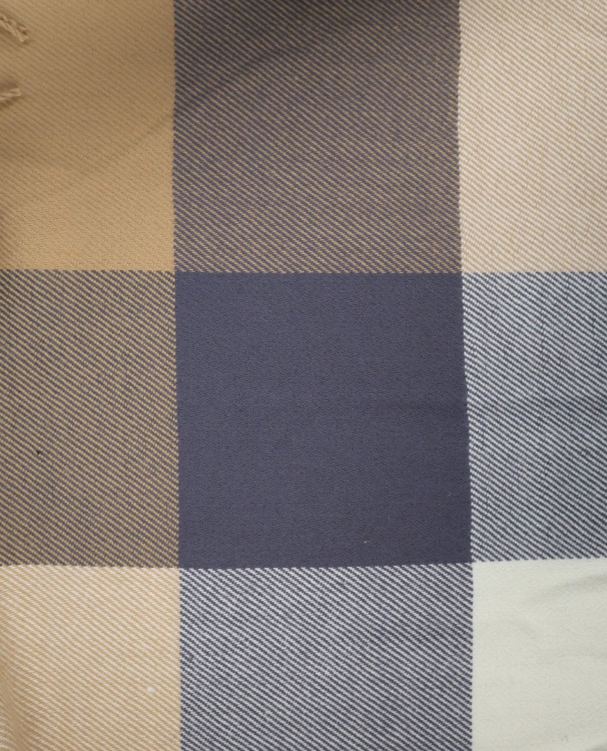 A close-up of a plaid fabric pattern with intersecting blocks of beige, navy blue, gray, and off-white, showing a woven texture.