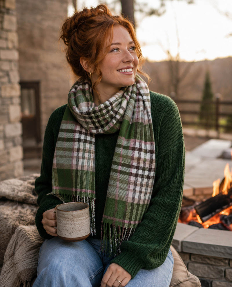 Woman wearing a green plaid scarf and holding a mug by a fireplace