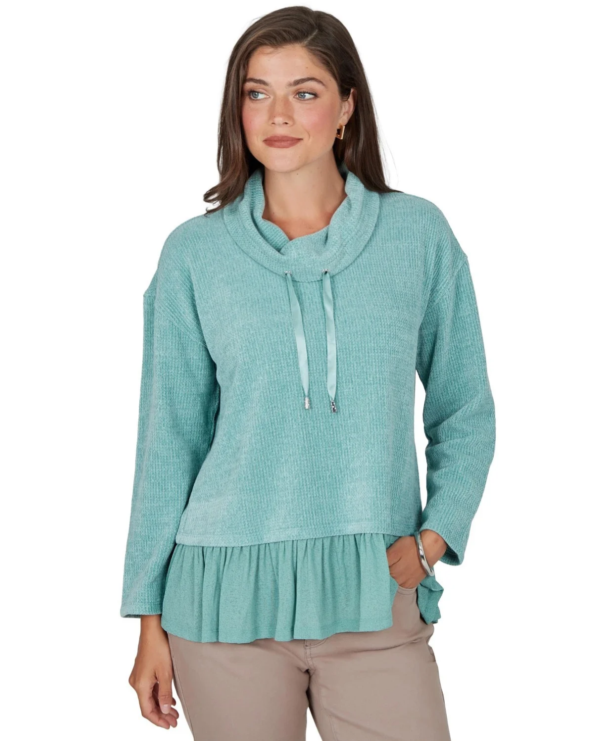 A woman wearing a light teal long-sleeve knit top with a cowl neck, drawstring detail, and a ruffled hem, paired with beige pants, against a plain white background.