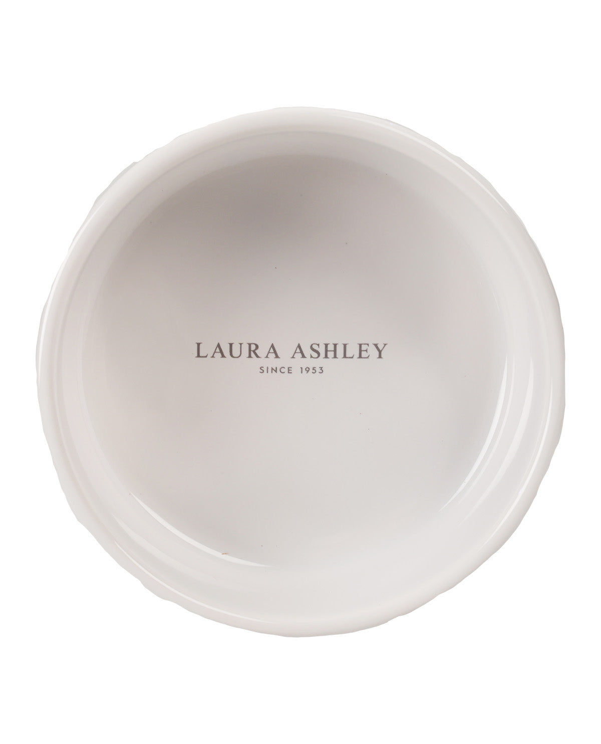 A top-down view of a white ceramic plate with a scalloped rim, featuring the text 'LAURA ASHLEY SINCE 1953' printed in gray in the center.