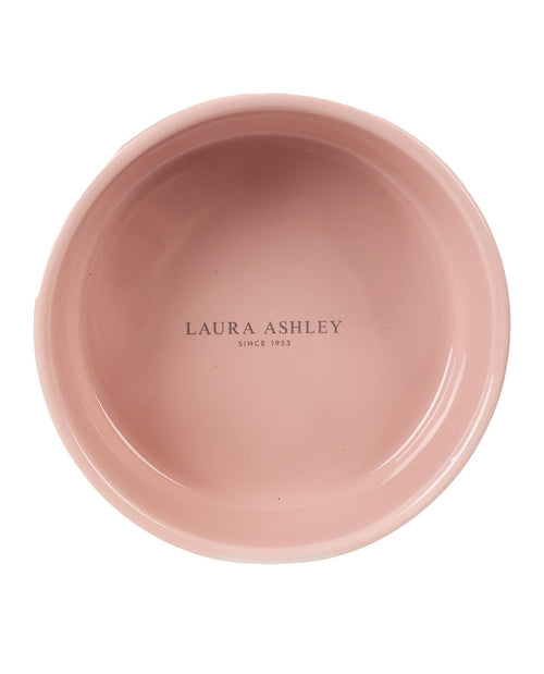 A top-down view of a dusty pink ceramic bowl with 'LAURA ASHLEY SINCE 1953' printed in black in the center, isolated on a white background.