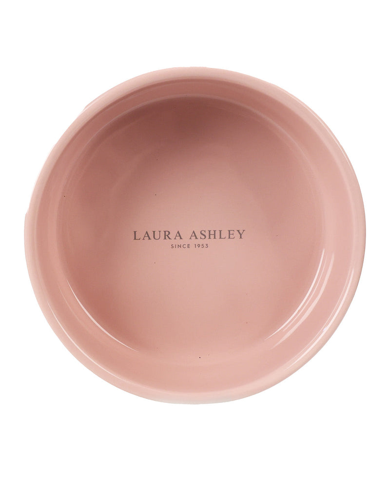 A top-down view of a dusty pink ceramic bowl with 'LAURA ASHLEY SINCE 1953' printed in black in the center, isolated on a white background.