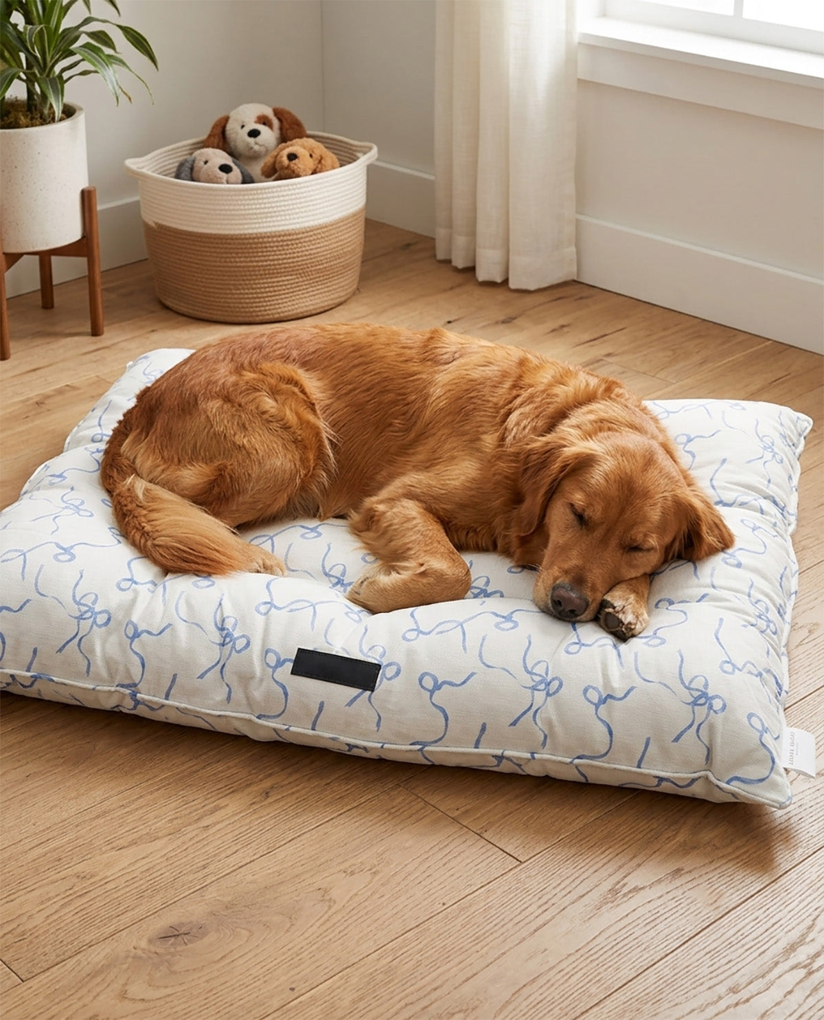 A golden retriever dog sleeping comfortably on a white rectangular dog bed with a blue abstract line pattern, placed on a light wood floor in a bright room.