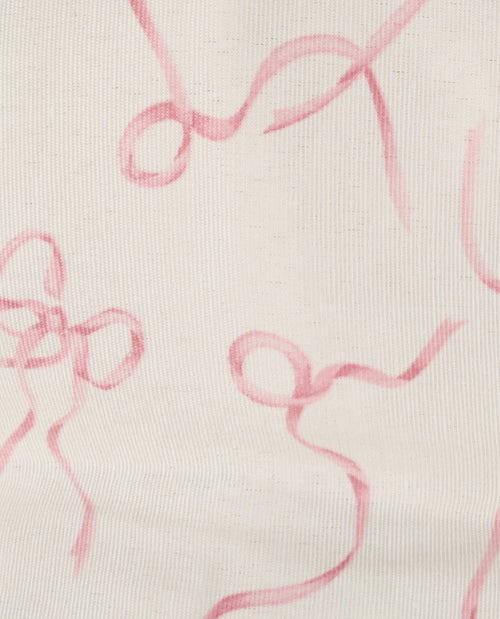 A close-up of a light cream fabric with a pink abstract ribbon or bow print.