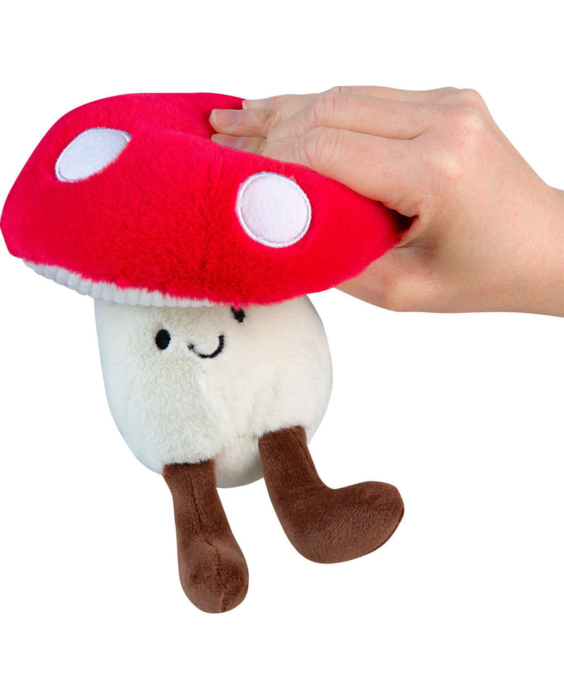 Plush toy mushroom with a red cap and white spots, held by a hand on a white background