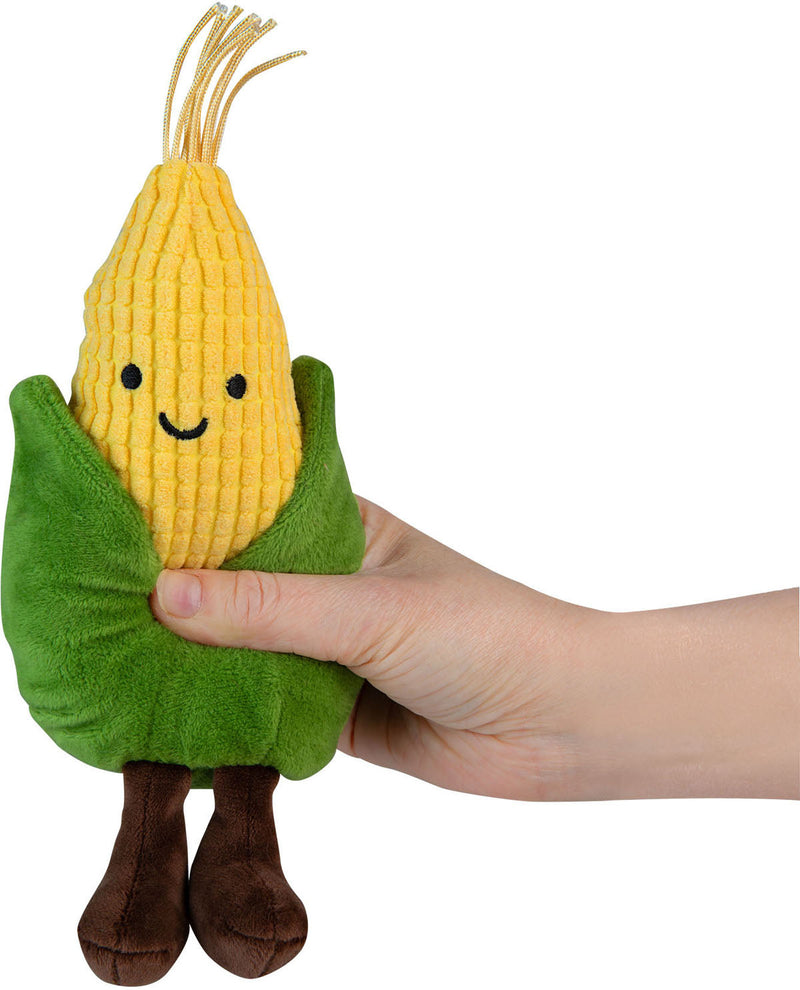 Plush toy corn on the cob held by a hand against a white background
