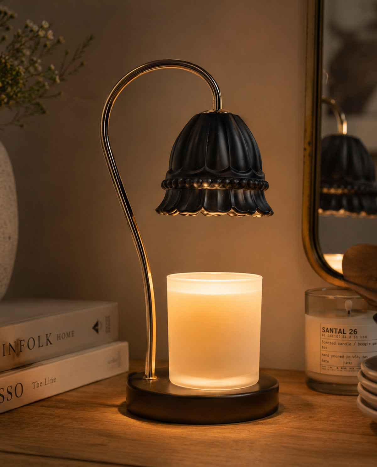 Decorative table lamp with a candle on a wooden surface, surrounded by books and a mirror.