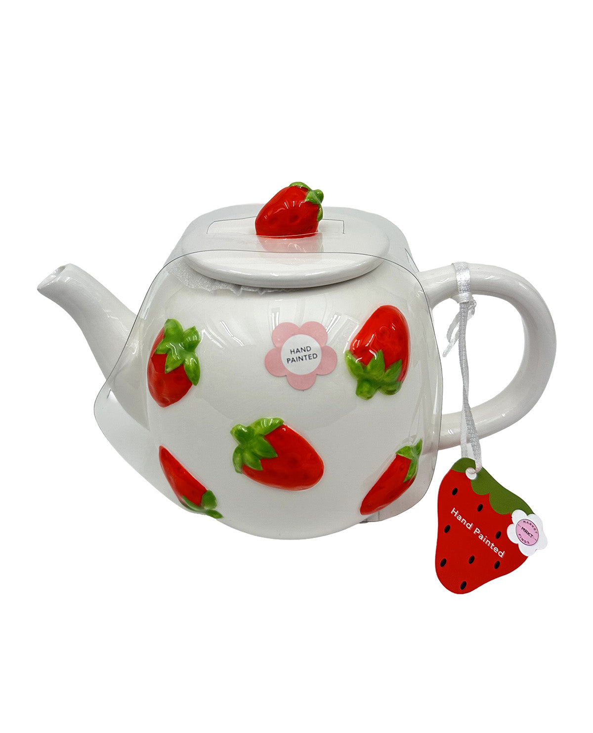 A white ceramic teapot decorated with 3D red strawberries with green tops, featuring a small pink flower badge that reads 'HAND PAINTED' and a matching strawberry-shaped tea tag hanging from the handle.