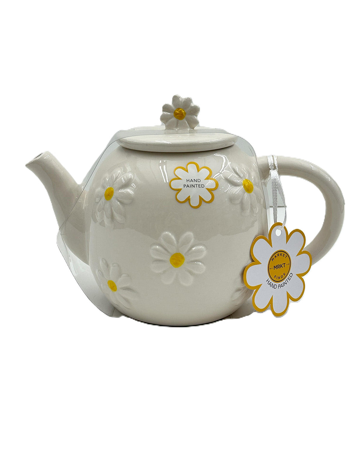 An off-white ceramic teapot decorated with embossed daisy flowers in white and yellow, featuring a matching lid with a flower knob and a hanging paper tag.