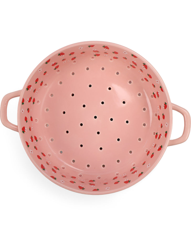 A pink enamel colander with small red strawberry patterns around the rim and handles, shown from a top-down view on a white background.