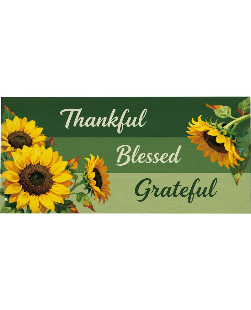 A rectangular decorative sign or print with the words 'Thankful Blessed Grateful' in white and dark green script over three horizontal green bands, decorated with large yellow sunflowers on the left and right sides.