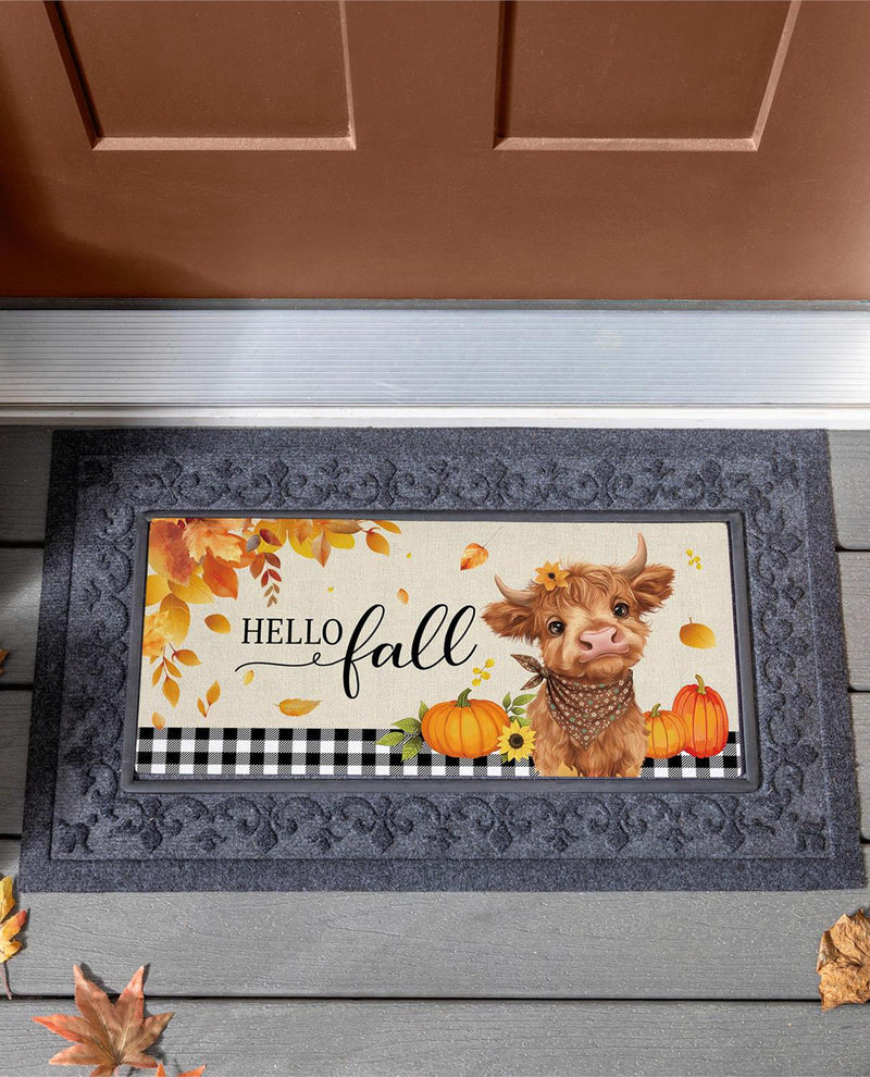 A rectangular doormat with a decorative autumn design, placed in front of a brown door on a gray porch. The mat features the words 'Hello fall' with a cow illustration, pumpkins, fall leaves, and a black-and-white buffalo plaid stripe near the bottom.