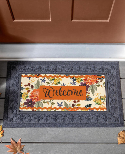 An autumn-themed doormat with a dark gray border and a colorful floral center featuring the word 'Welcome' in script, placed in front of a brown door on a gray porch.