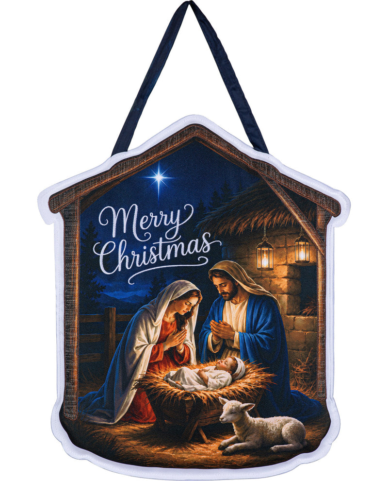A house-shaped Christmas ornament featuring a nativity scene with Mary, Joseph, baby Jesus in a manger, and a lamb under a star, with the words 'Merry Christmas' in white script. The ornament has a white border and dark blue hanging straps, shown on a plain white background.