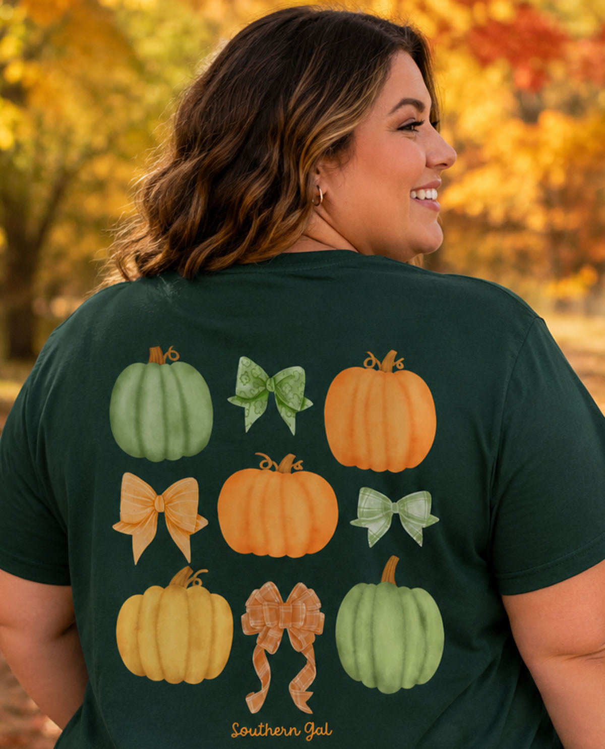 Person wearing a green t-shirt with pumpkin and bow designs in an autumn setting
