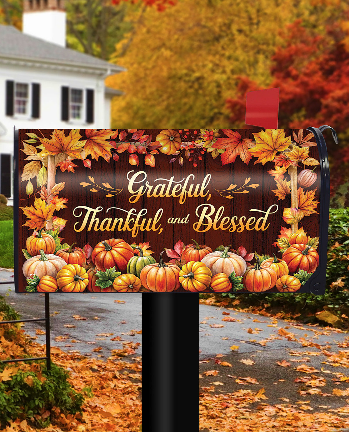 A decorative autumn-themed mailbox cover displayed on a black mailbox post in a residential outdoor setting. The cover features the text 'Grateful, Thankful, and Blessed' in gold script over a dark wood background, surrounded by colorful fall leaves, pumpkins, and gourds.