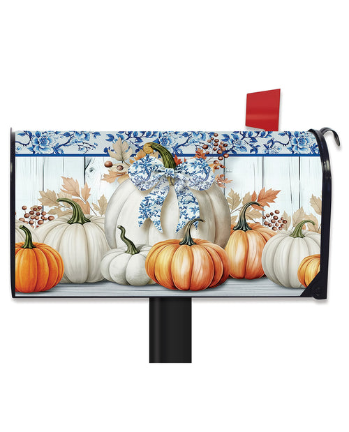 A decorative mailbox cover featuring a fall harvest design with orange and white pumpkins, blue floral border details, and a blue bow, shown mounted on a black mailbox against a white background.