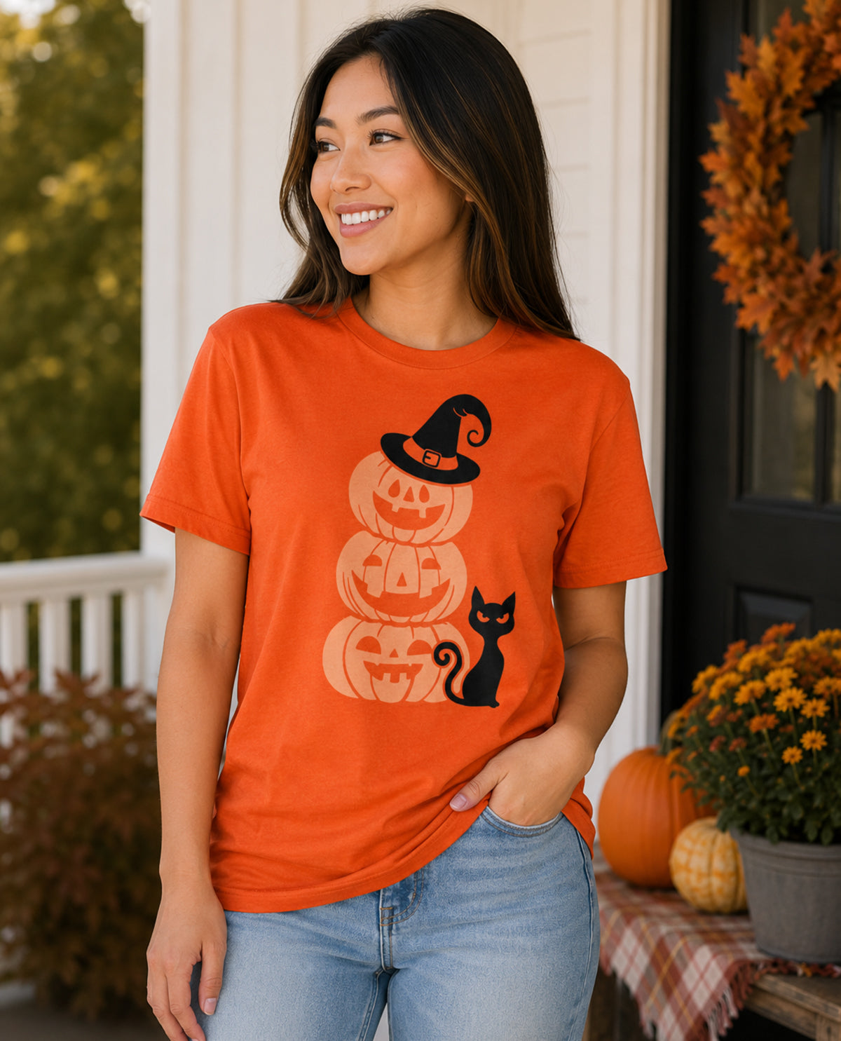 Woman wearing an orange t-shirt with Halloween design on a porch decorated for fall.