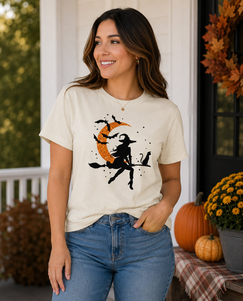 Woman wearing a t-shirt with a witch and pumpkin design on a porch with pumpkins and fall decorations.