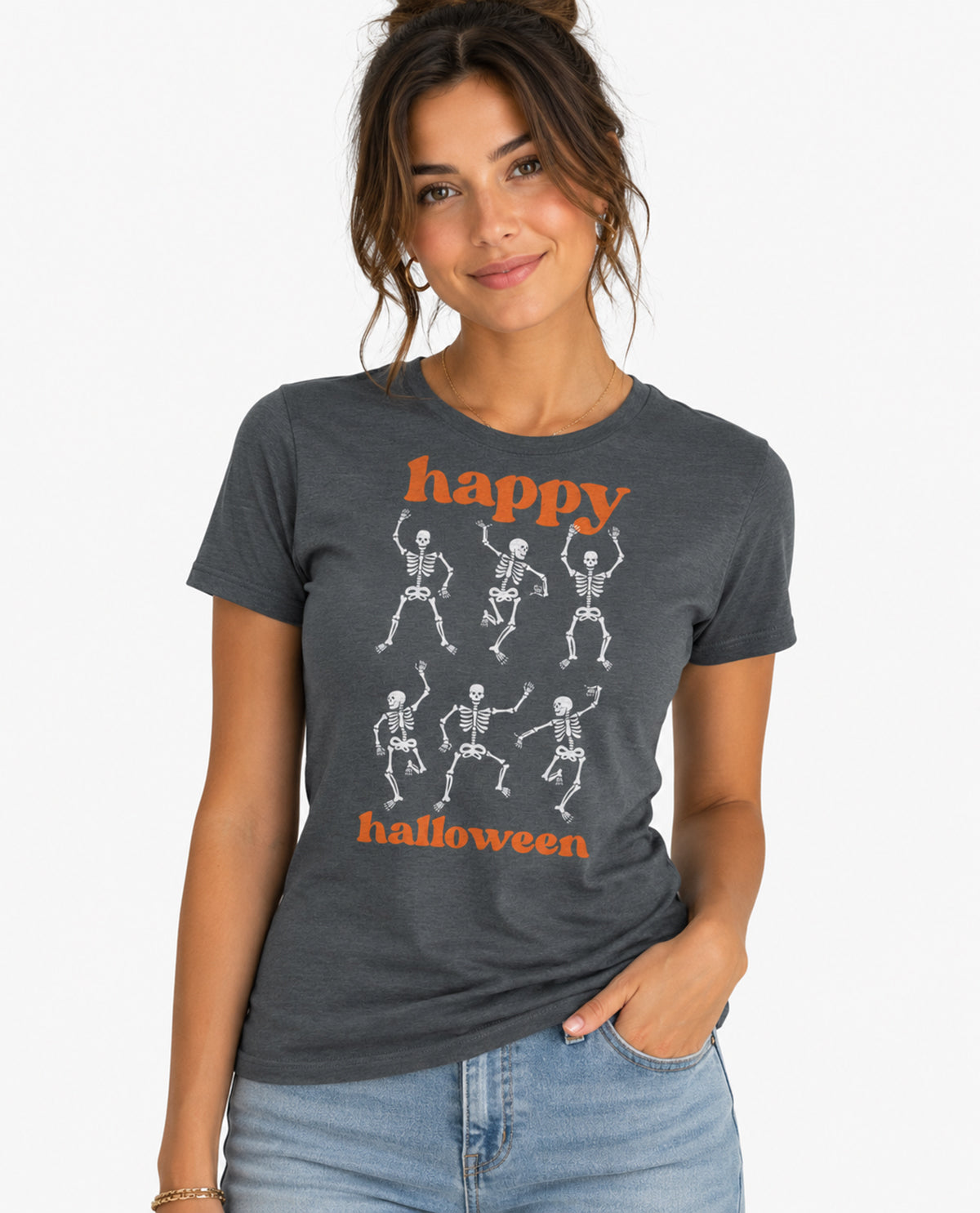 A woman wearing a dark heather gray graphic t-shirt with 'happy halloween' printed in orange and white dancing skeletons, paired with light blue jeans against a plain white background.