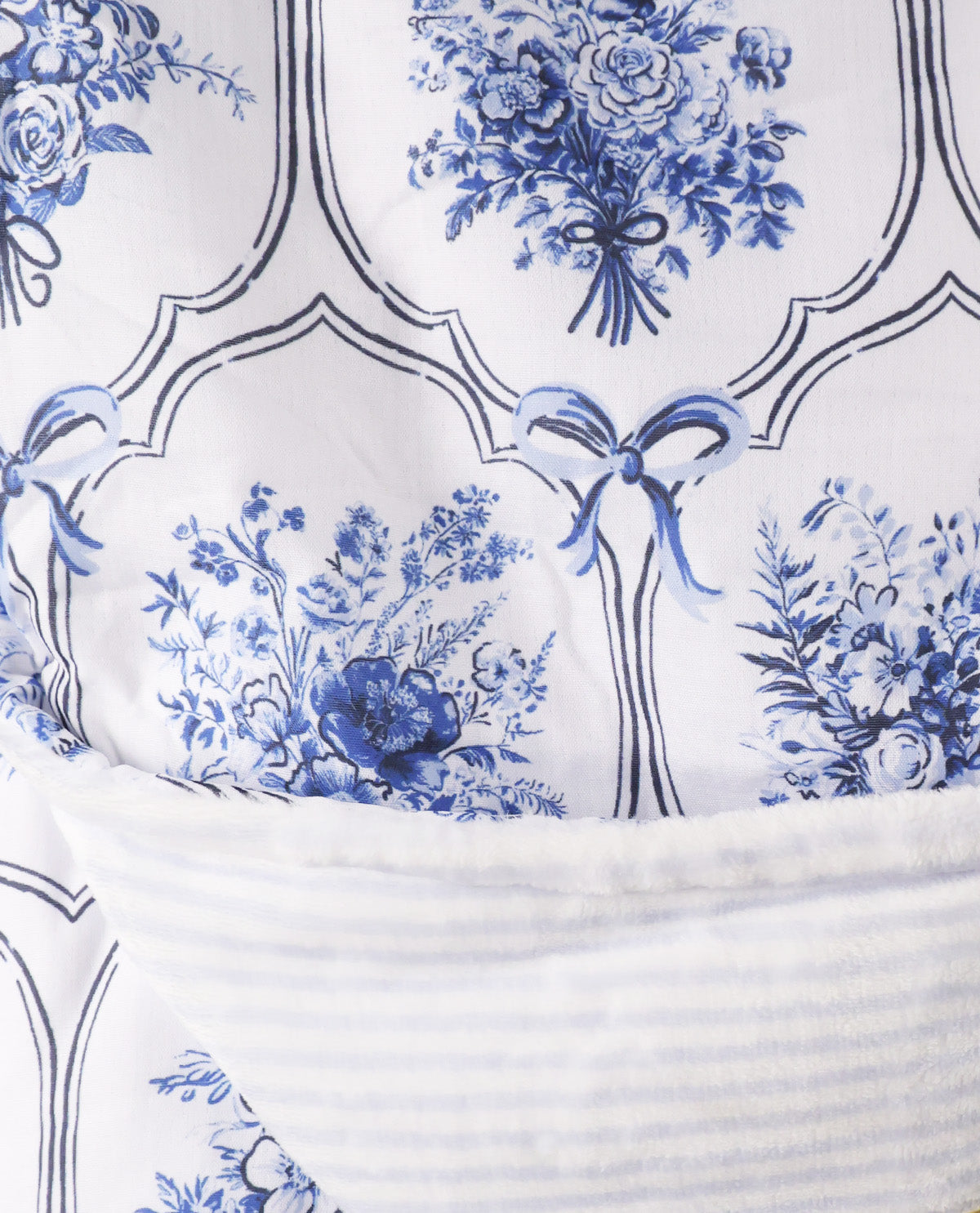Close-up of a white textile with a blue floral toile pattern and a ribbed white fabric section layered over it.