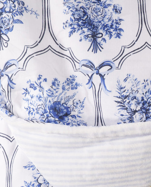 Close-up of a white textile with a blue floral toile pattern and a ribbed white fabric section layered over it.