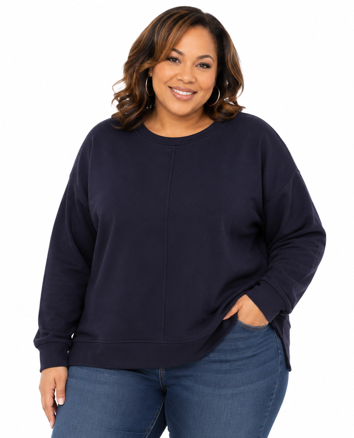 A woman wearing a dark navy blue crewneck sweatshirt and blue jeans, standing against a plain white background.