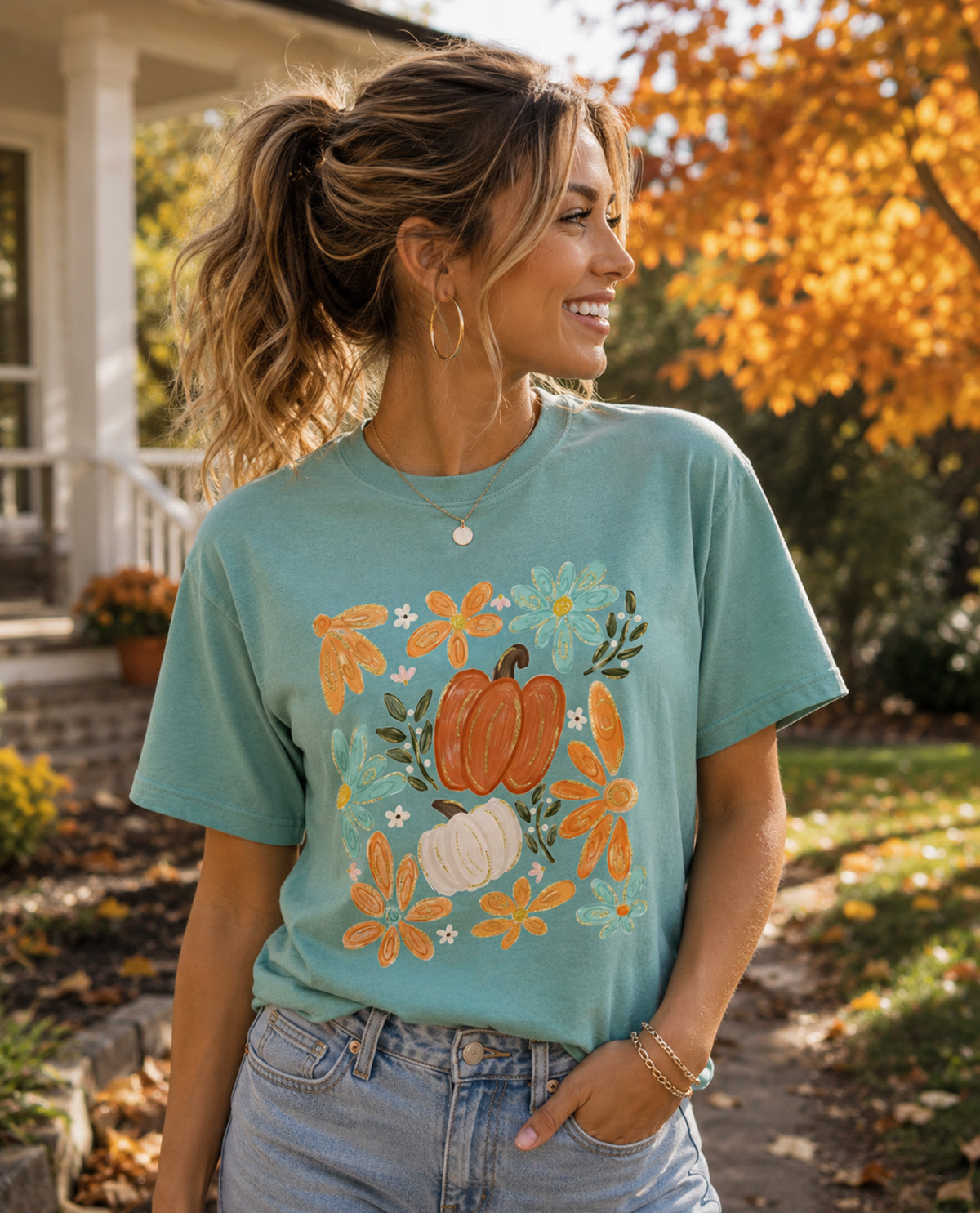 Woman wearing a teal t-shirt with pumpkin design outdoors in autumn.