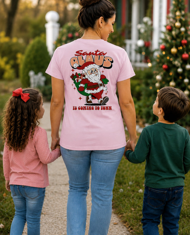 Woman wearing a pink t-shirt with Santa Claus graphic and text, standing with two children outdoors.